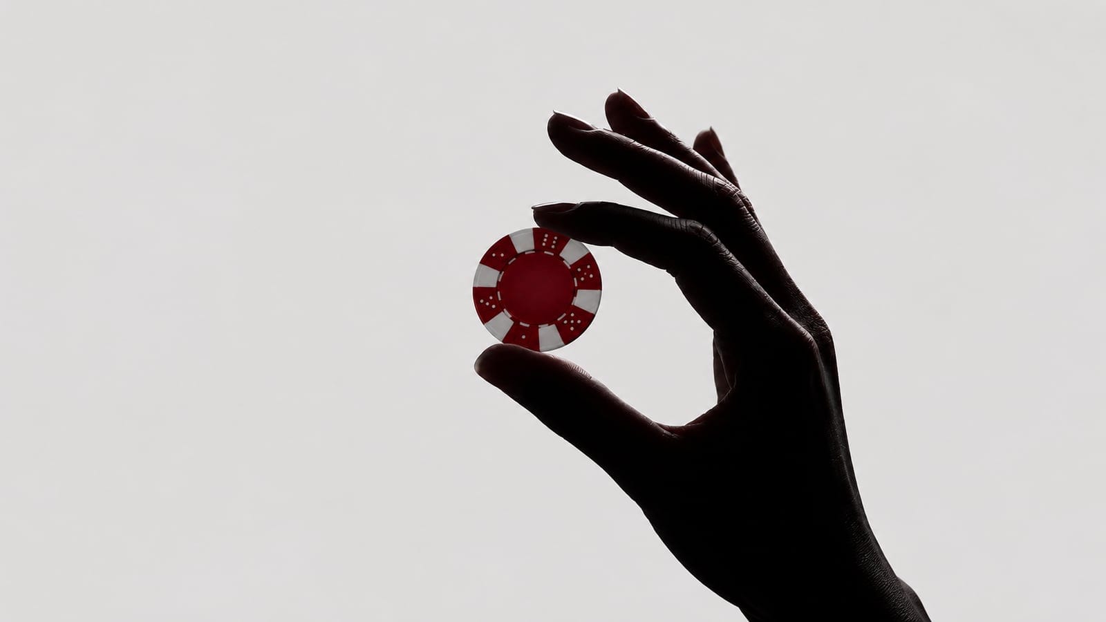 A hand holding a single red poker chip against a deep red background